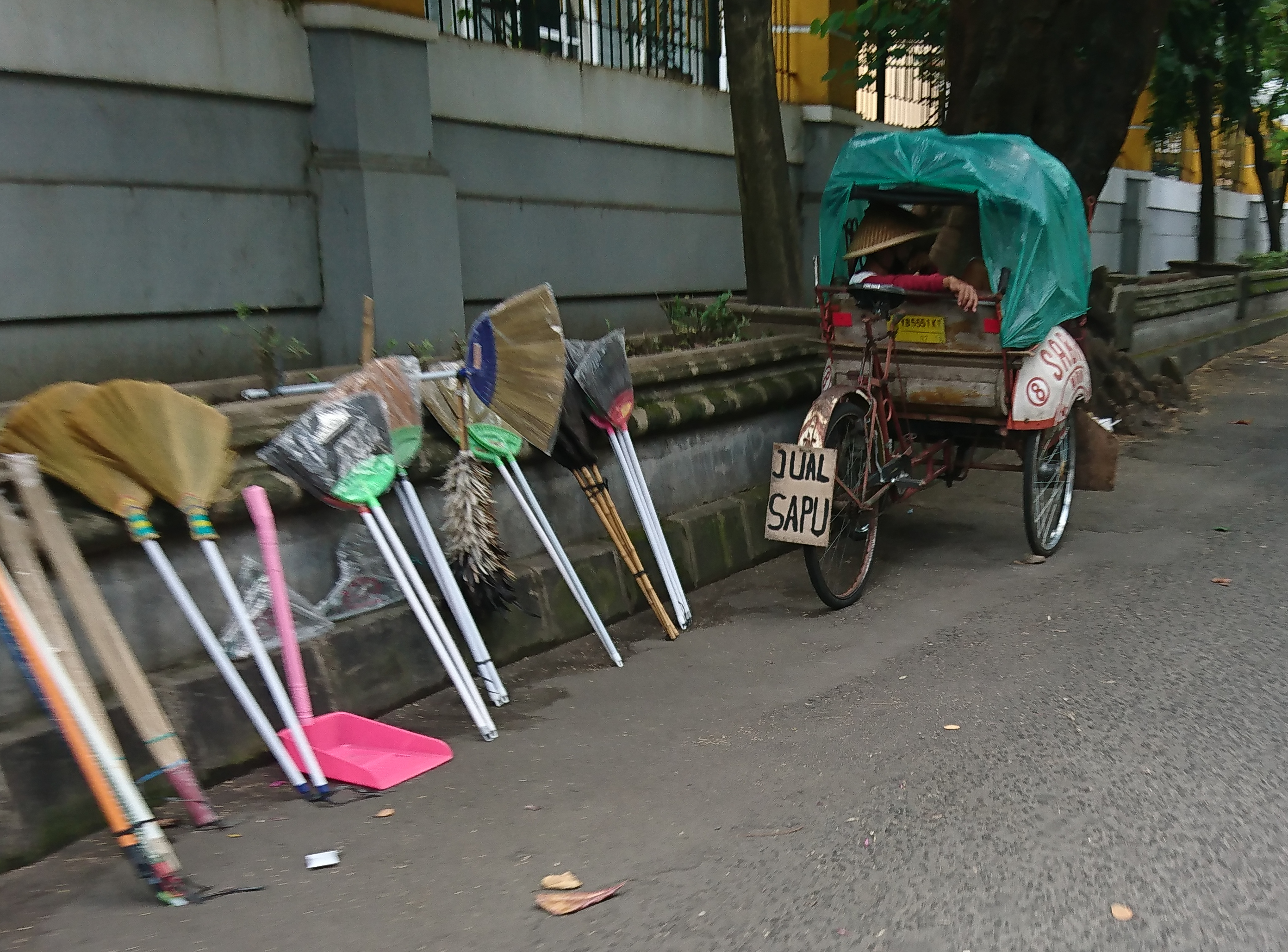 Pengayuh Becak Menjajakan Sapu Gelagah Sembari Menunggu Penumpang