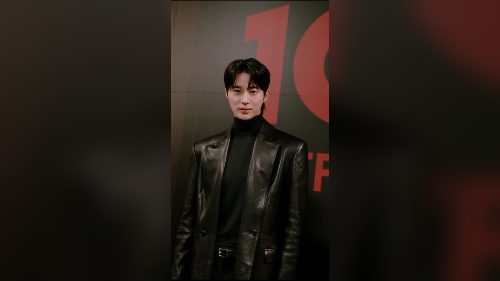 Byeon Woo-seok berjaket kulit hitam berpose di depan papan Netflix Korea 10 tahun