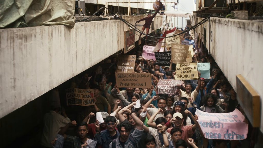 Massa mahasiswa berdemonstrasi membawa poster di lorong jalan dalam film Laut Bercerita