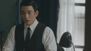 Park Jin-young sebagai Sato Hideo duduk di meja kerja dalam drama 100 Days of Deception