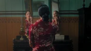 Perempuan berbaju merah bermotif bunga duduk di depan cermin dalam trailer film Pirunduk