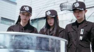 Tiga member ILLIT bertopi seragam agen dalam MV You're Under Arrest
