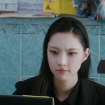 Member ILLIT berjas hitam duduk di depan monitor dalam teaser You're Under Arrest