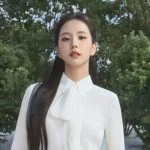 Jisoo BLACKPINK tersenyum memakai blus putih berpita di luar ruangan