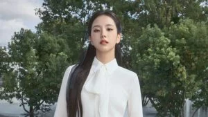 Jisoo BLACKPINK tersenyum memakai blus putih berpita di luar ruangan