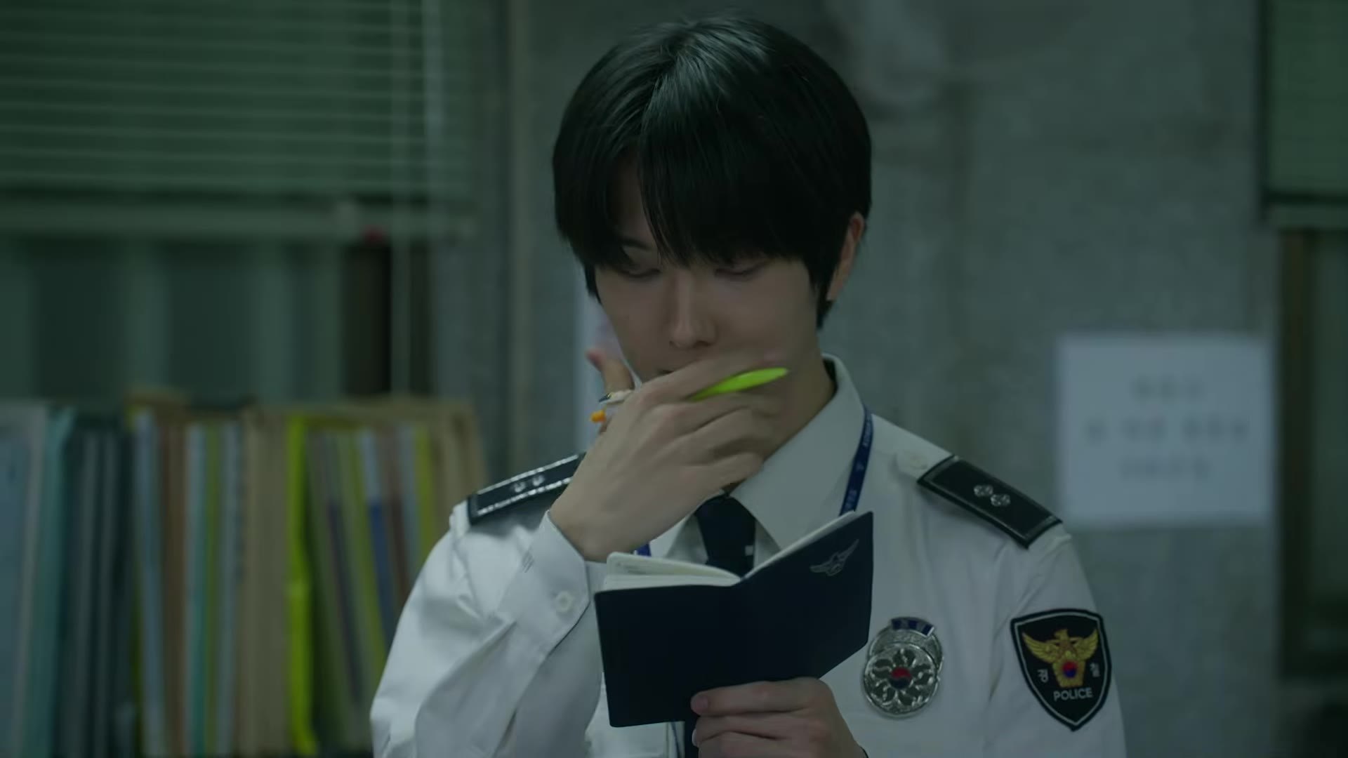 Jisung NCT sebagai Ji Dae-se memegang pulpen dan buku catatan dengan seragam polisi