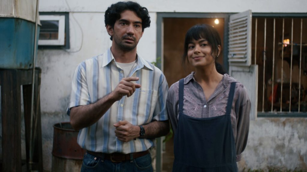 Reza Rahadian sebagai Biru Laut berdiri di depan rumah dalam trailer resmi film Laut Bercerita