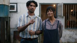 Reza Rahadian sebagai Biru Laut berdiri di depan rumah dalam trailer resmi film Laut Bercerita