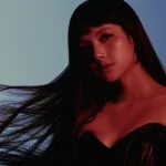 LISA berambut panjang tergerai dengan gaun korset hitam berlatar biru dalam visual PRESS PLAY