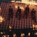 Keempat member LNGSHOT duduk di atap merah yang terbakar di tengah air dalam MV Masterpiece