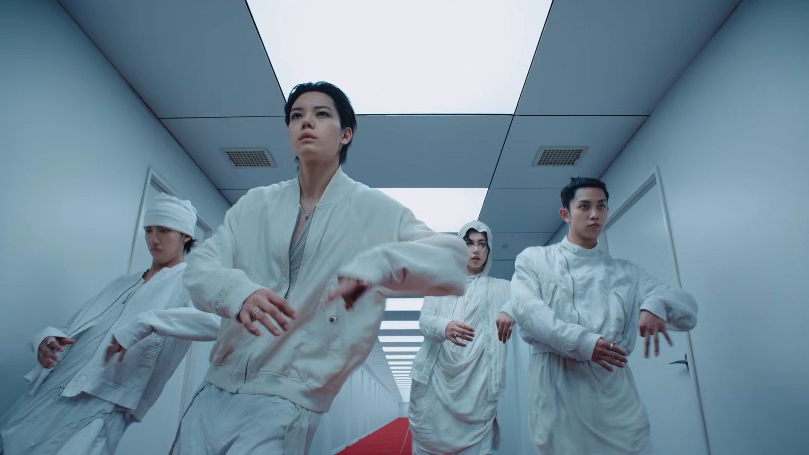 Member LNGSHOT berkostum putih menari di lorong putih berkarpet merah dalam MV Masterpiece