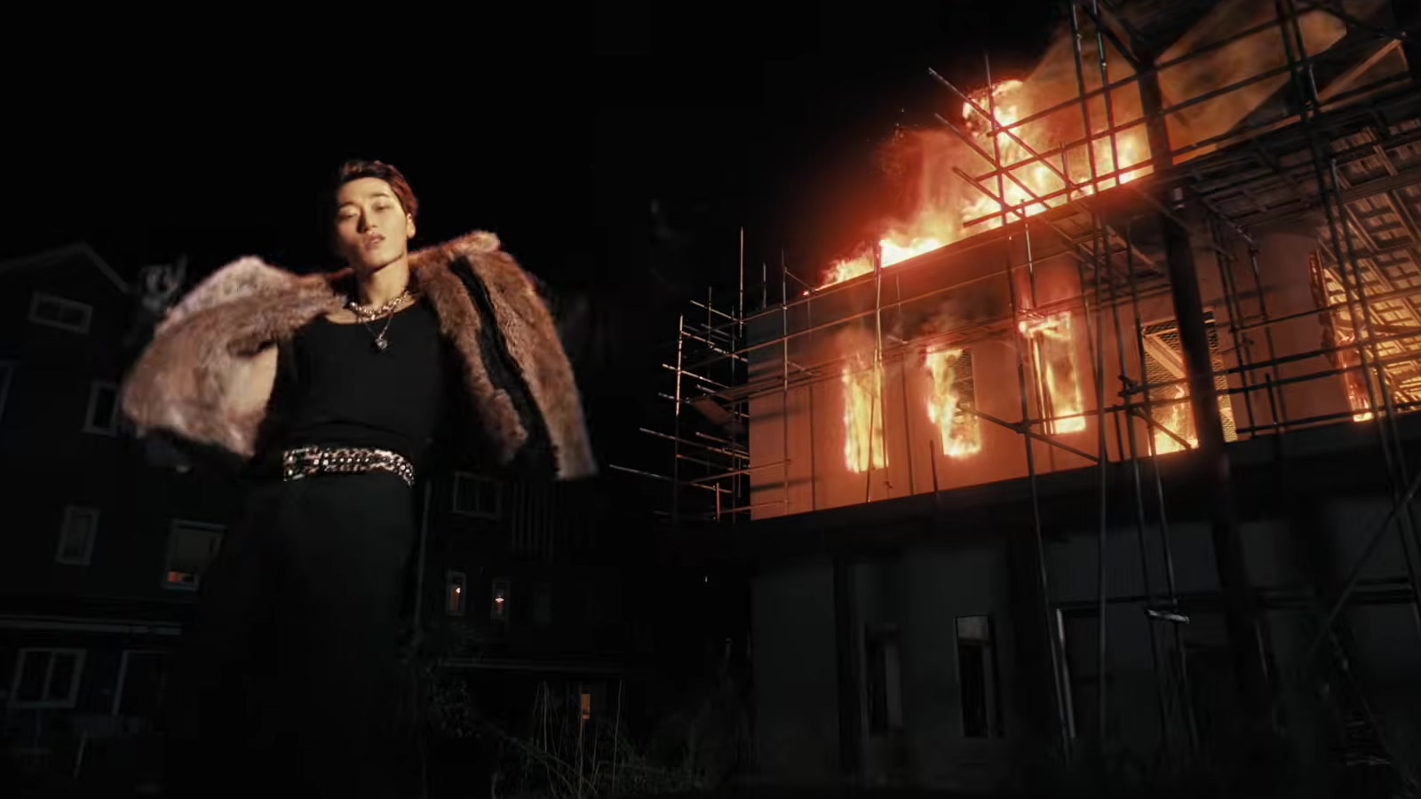 Member ATEEZ bermantel bulu berdiri di depan gedung terbakar dalam MV Drip