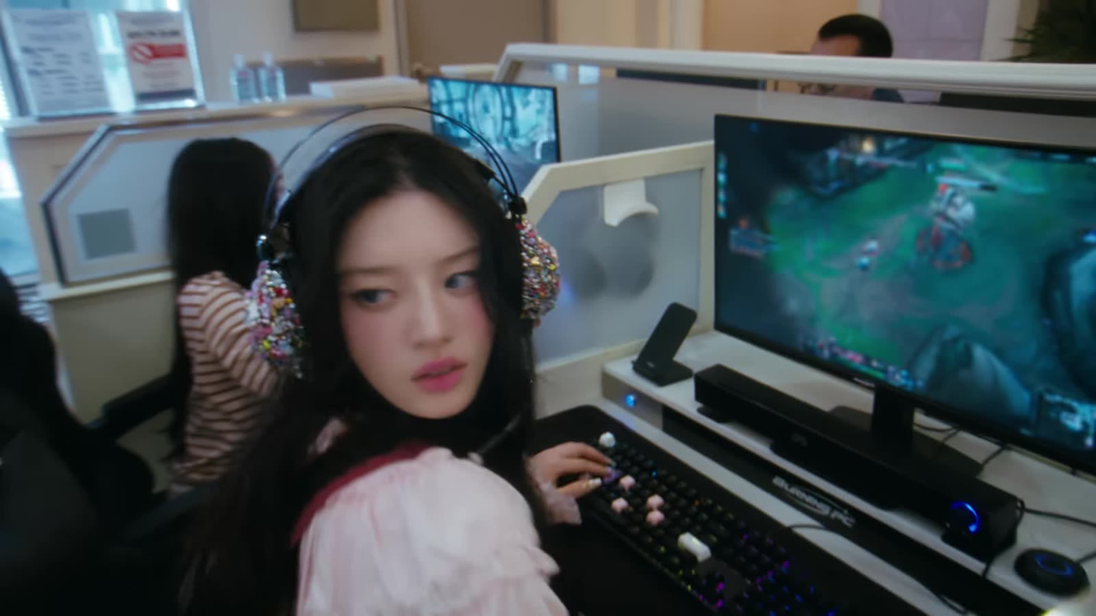 Member ILLIT memakai headset di depan komputer warnet dalam MV You're Under Arrest