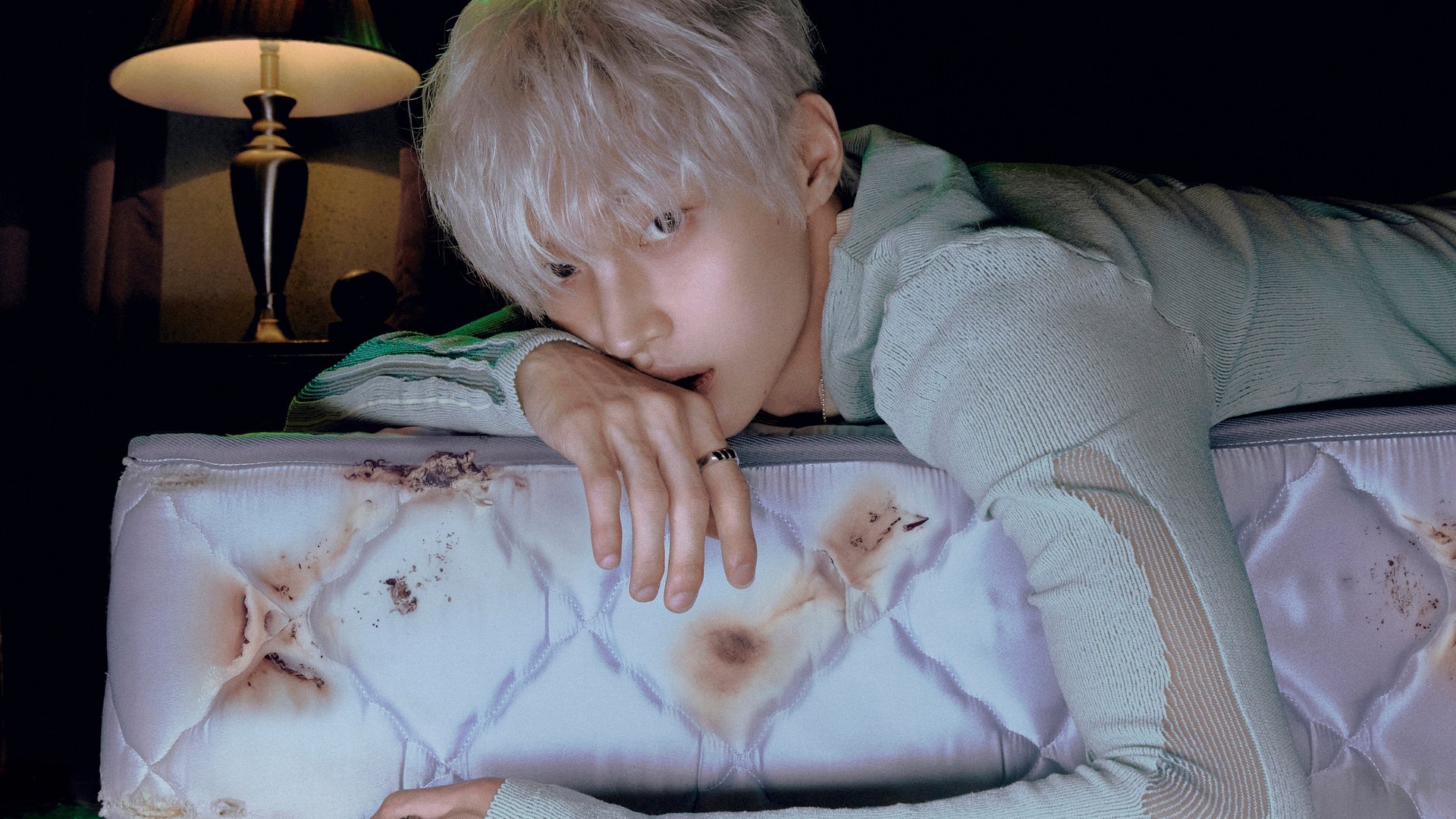 Member RIIZE berambut perak bersandar di kasur bernoda gosong dalam MV image Insomnia