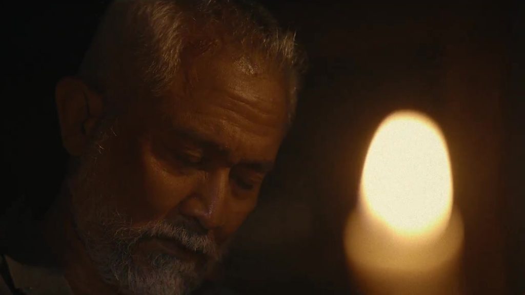 Eyang menunduk di dekat cahaya lilin dalam trailer film Serangan Balik Netflix