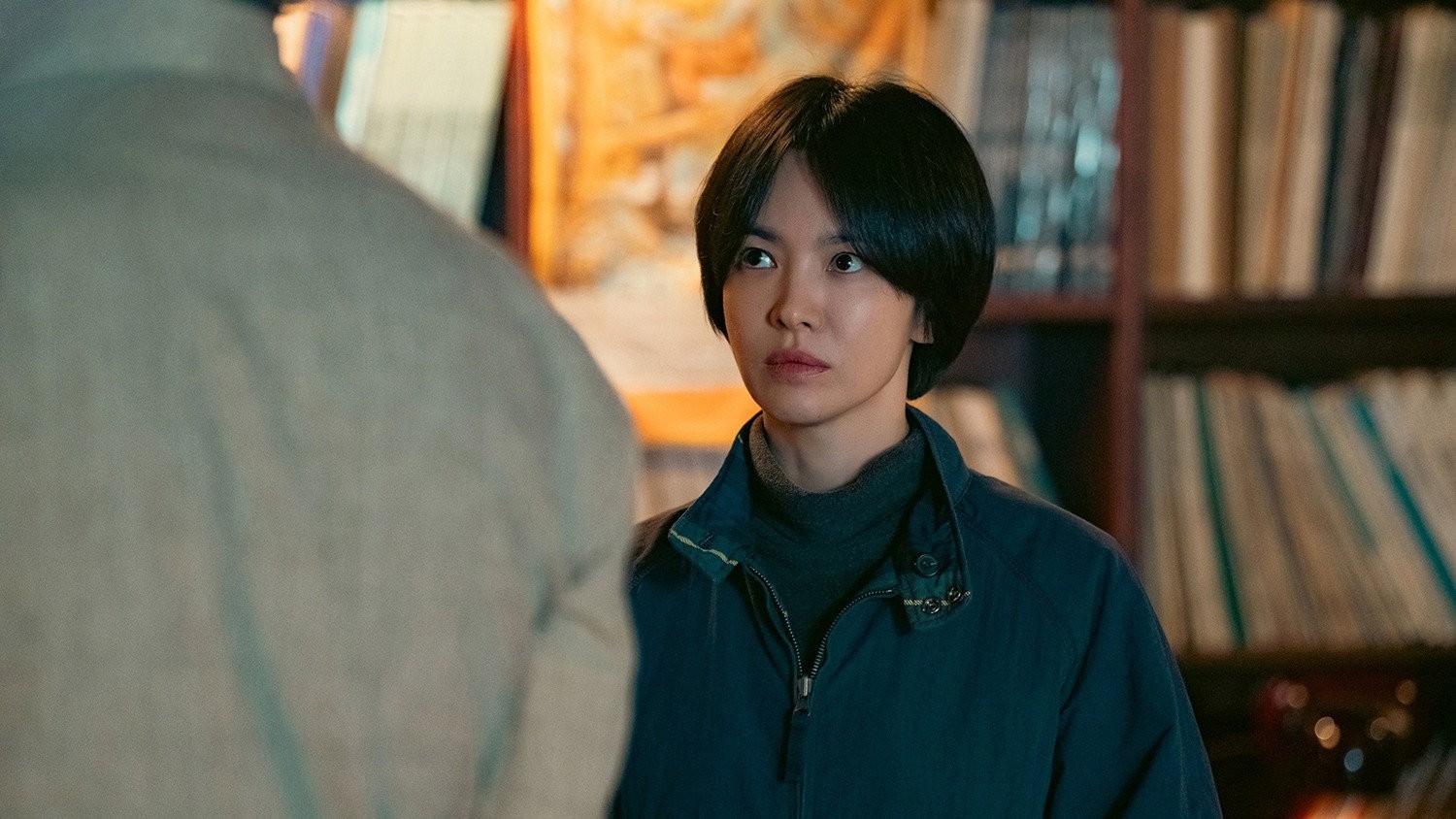 Song Hye-kyo sebagai Min-ja di sebuah ruangan berlatar rak dalam serial Tantara